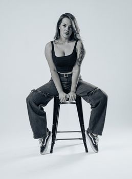 Fashionable woman with tattoos poses indoors in blue jeans and black top.