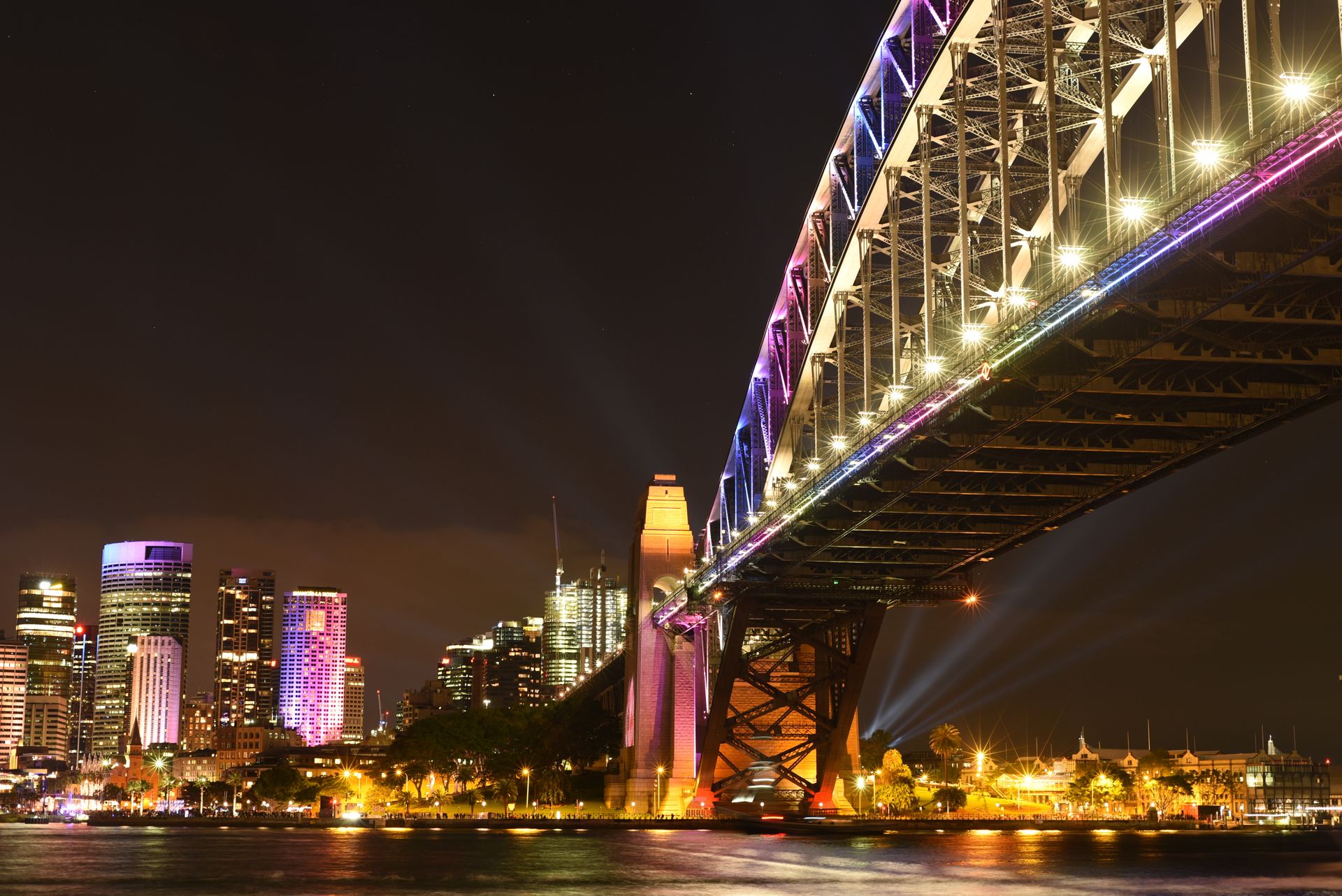 Sydney Harbour Bridge at night with the illuminated city skyline reflecting on the water.
