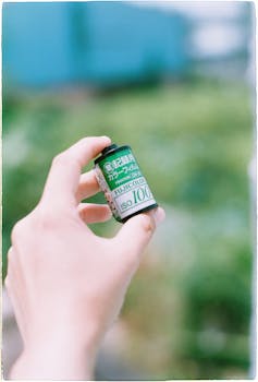 A close-up of a hand holding a Fuji ISO 100 film roll in an outdoor setting.