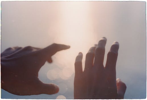 Abstract silhouette of hands reaching out towards soft sunlight, creating a dreamy effect.