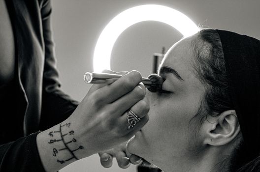 A makeup artist applies professional makeup to a woman with a brush in a studio setting.