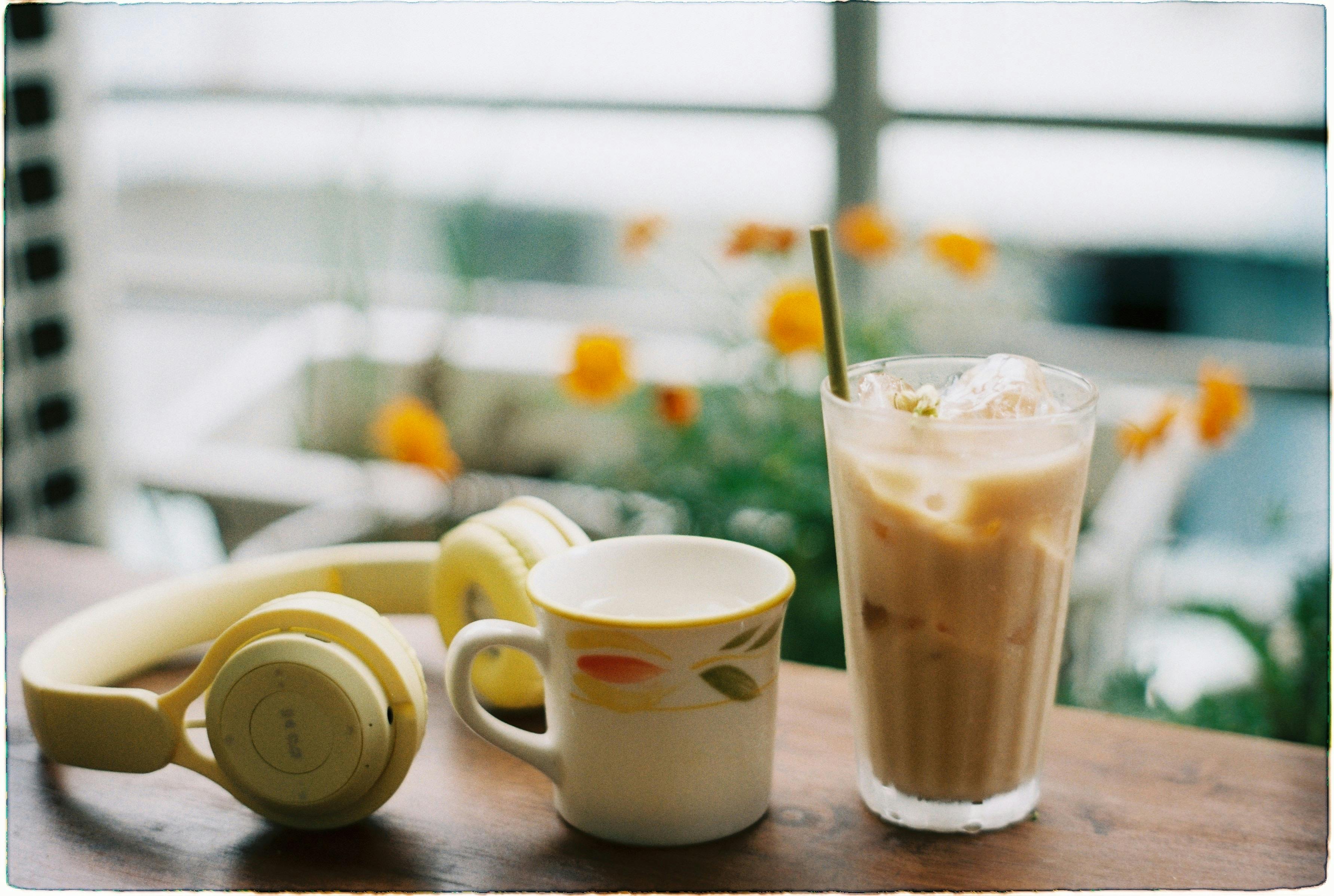 Iced coffee beside headphones and mug on a table in a bright setting.