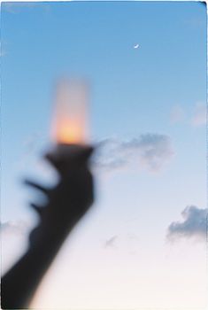 Silhouette of a hand with candle against sky and crescent moon.