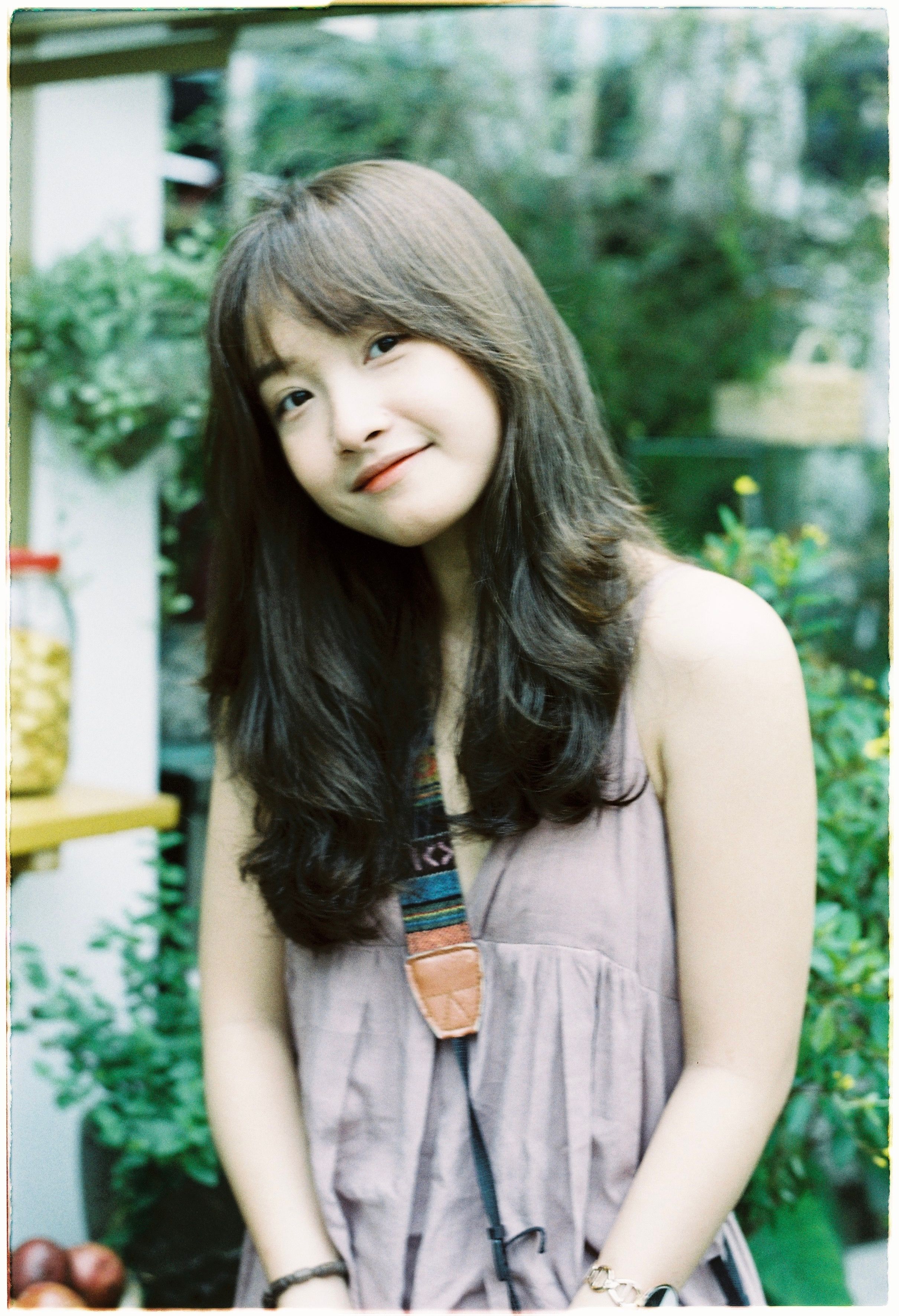 Charming portrait of a young woman outdoors with lush greenery.