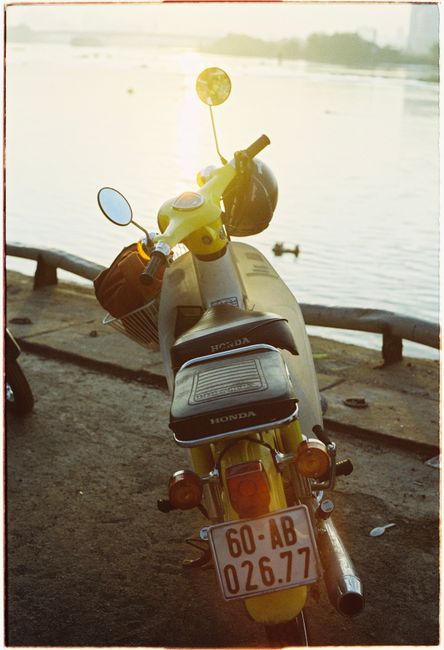 Vintage yellow scooter parked by the riverside bathed in warm sunset light.