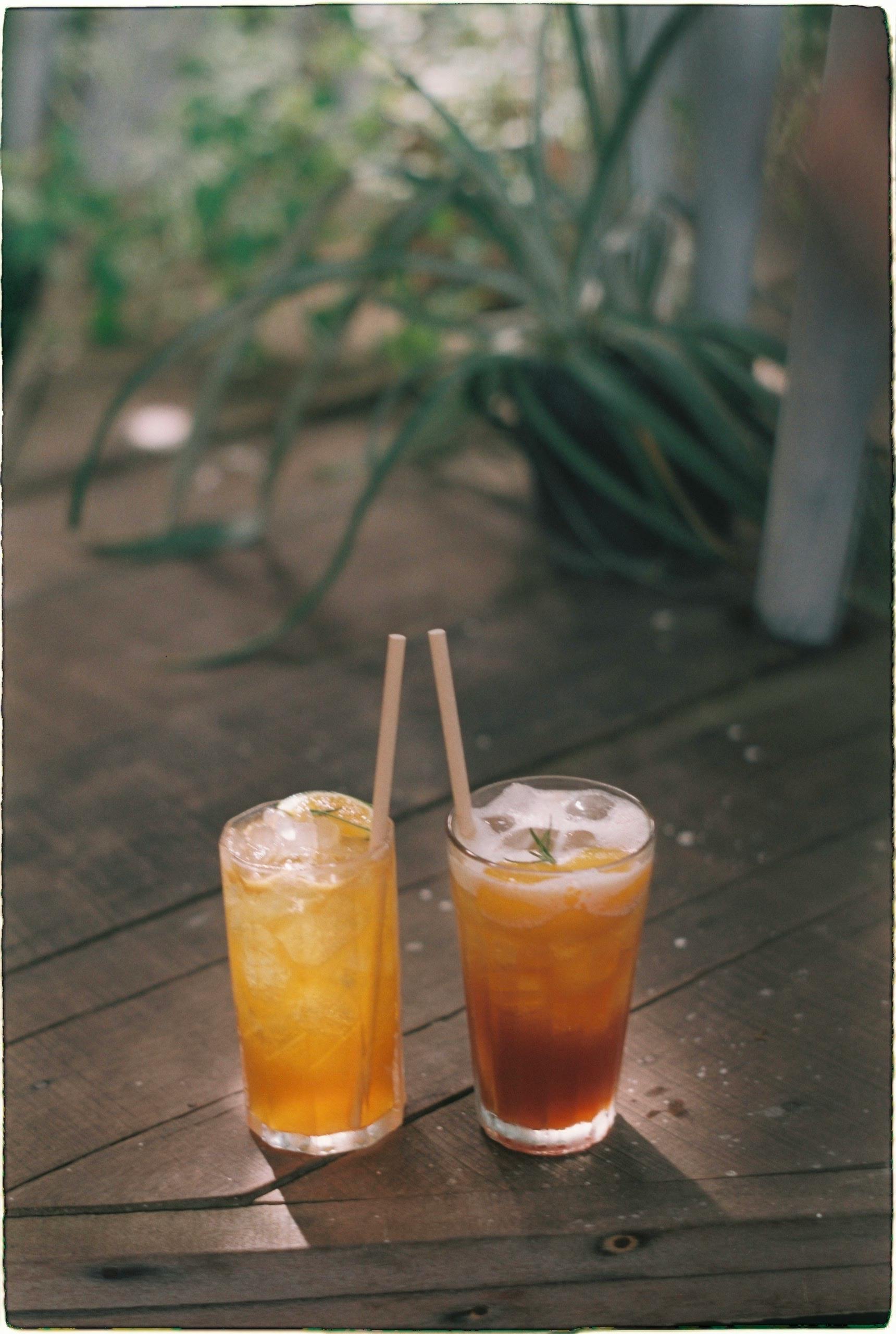 Two iced tea glasses with straws on a rustic wooden table in a relaxed outdoor setting.
