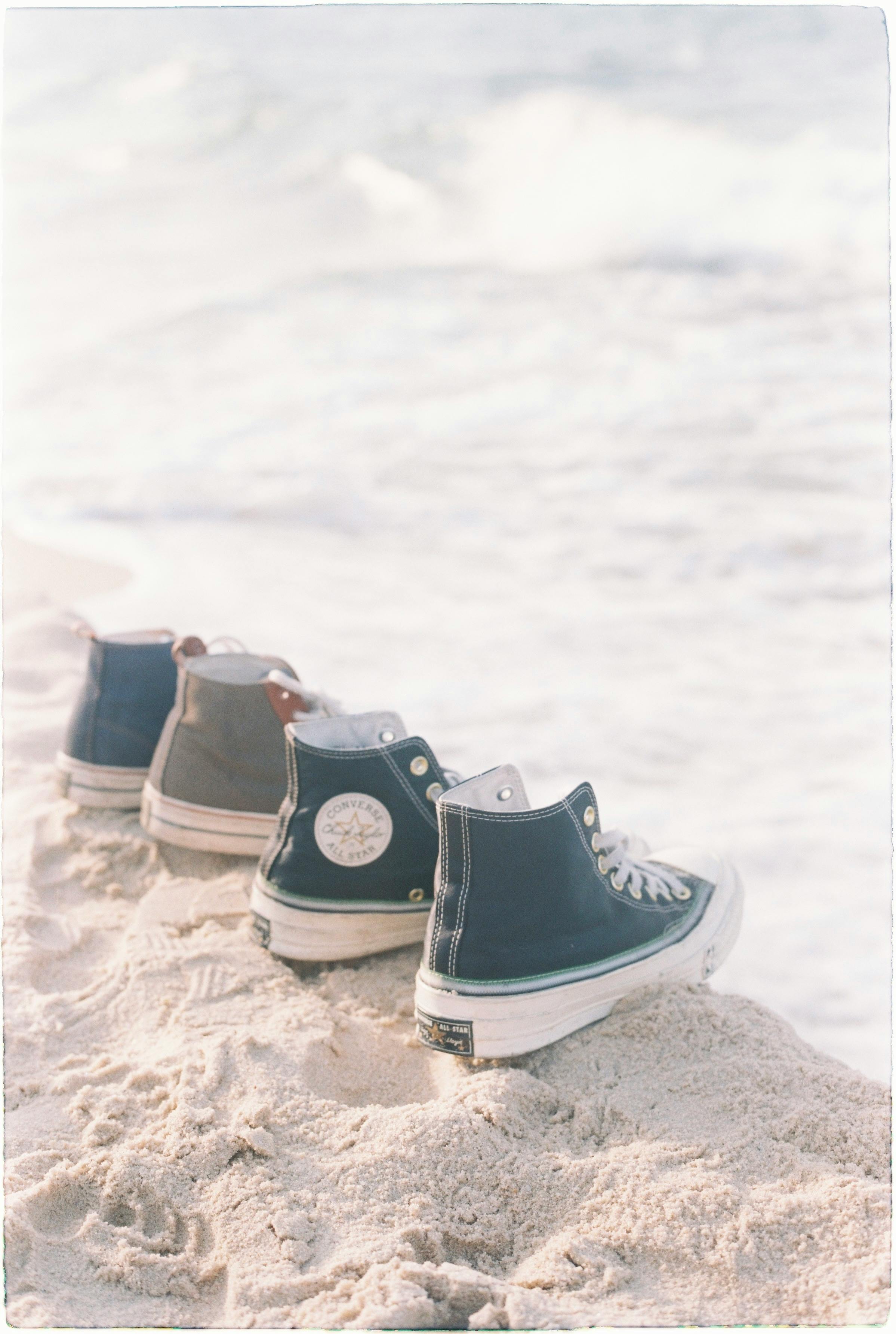 Classic high-top sneakers lined up on a sandy beach, waves in the background.
