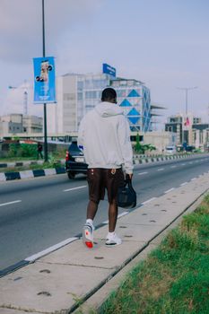 Man walks along city sidewalk, modern architecture in backdrop.