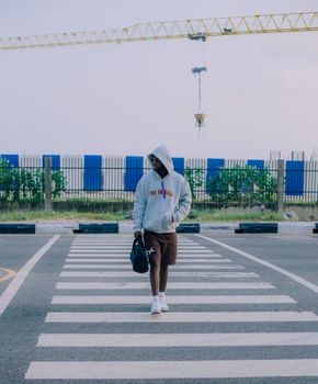 A person in a hoodie and shorts casually walks across a crosswalk, carrying a bag.