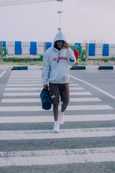 Man in a hoodie and shorts walking across a city street crosswalk. Casual urban fashion.