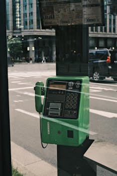 A green public payphone against a city street backdrop, reflecting urban nostalgia.