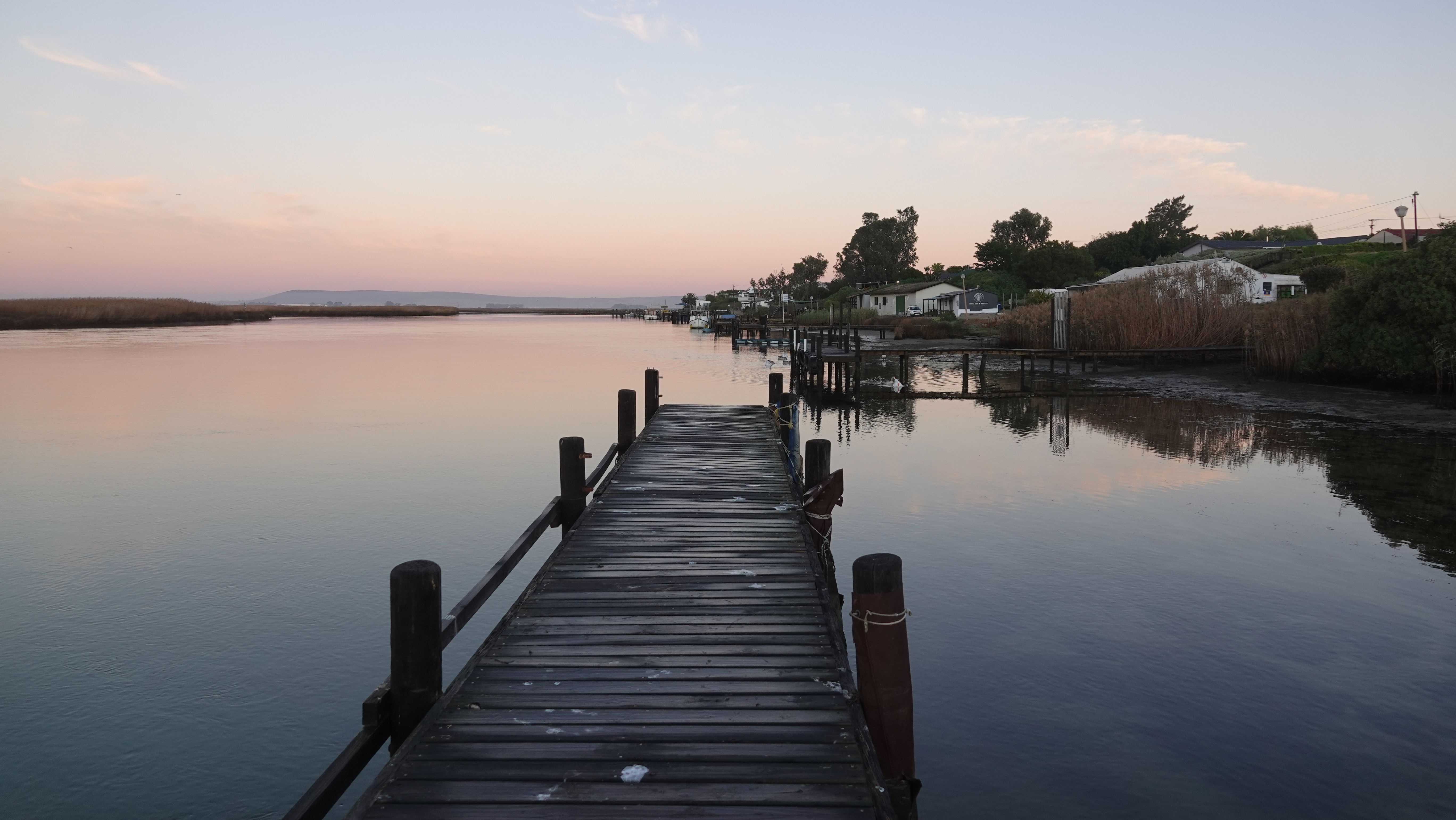 Peaceful view of a wooden dock by the river in Velddrif, South Africa at sunrise.