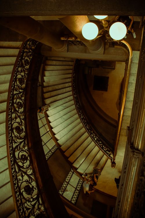 Free Aerial view of a grand spiral staircase with ornate railing in a historic building. Stock Photo