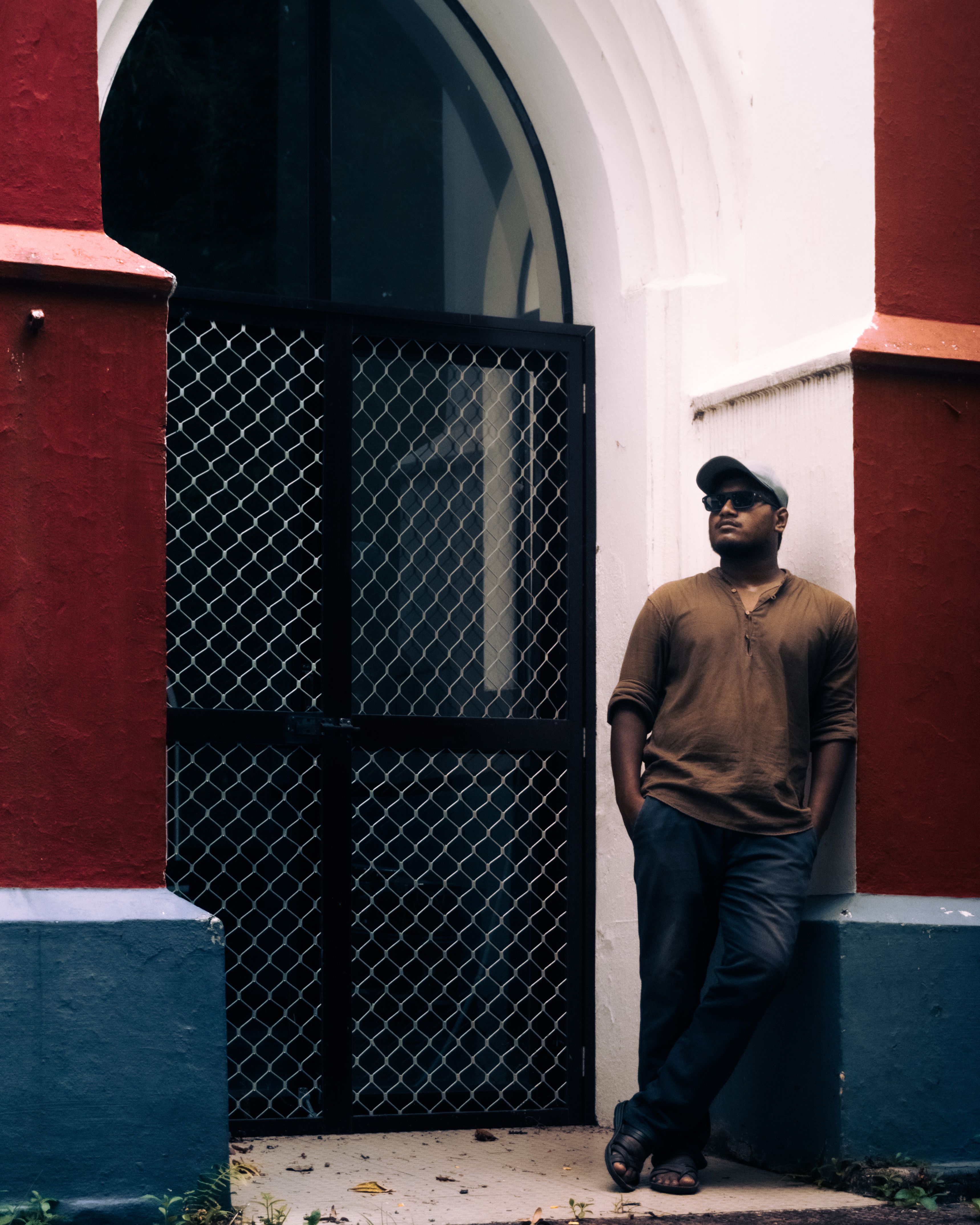 Casual man leaning against colorful building archway, urban style.
