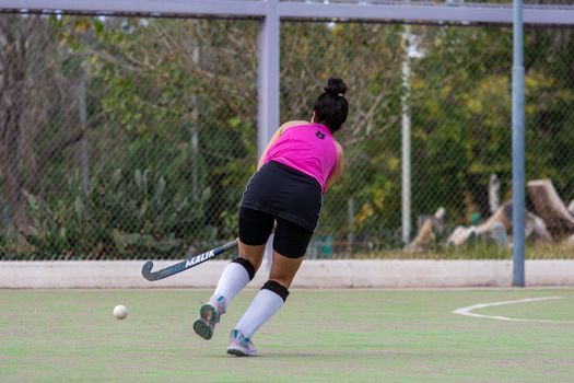 Back view of female field hockey player in motion on an outdoor field, wearing pink jersey.