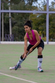 Focused young woman playing field hockey outdoors on a clear day.