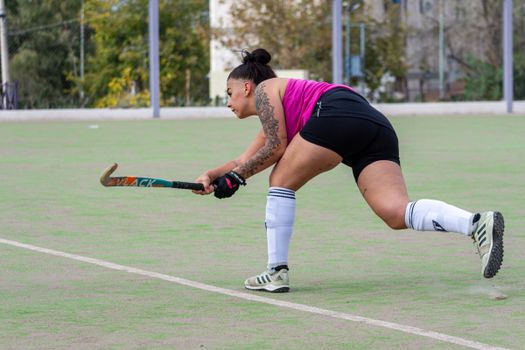 A female hockey player wearing a pink top playing field hockey on an outdoor pitch.