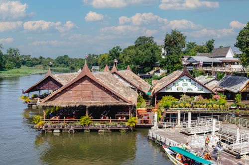 Free Charming riverside view of traditional Thai wooden houses over water, surrounded by lush greenery. Stock Photo