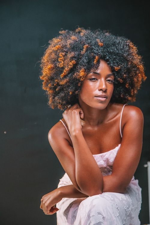 Free A striking portrait of a confident woman with vibrant curly hair and a thoughtful expression. Stock Photo