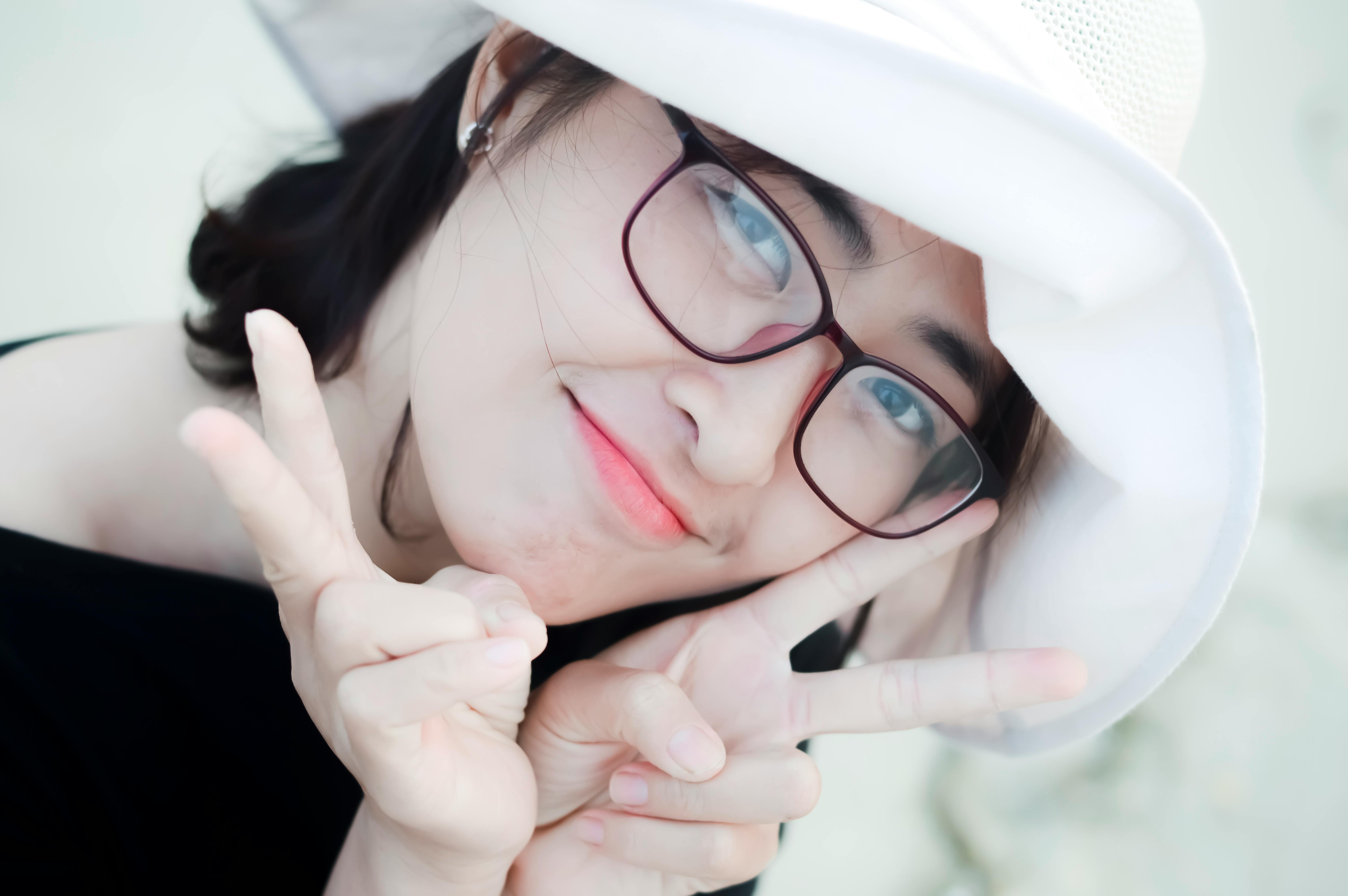 Ücretsiz Gözlük takan ve beyaz şapka takan, barış işareti yapan gülümseyen bir kadının parlak portresi. Stok Fotoğraflar