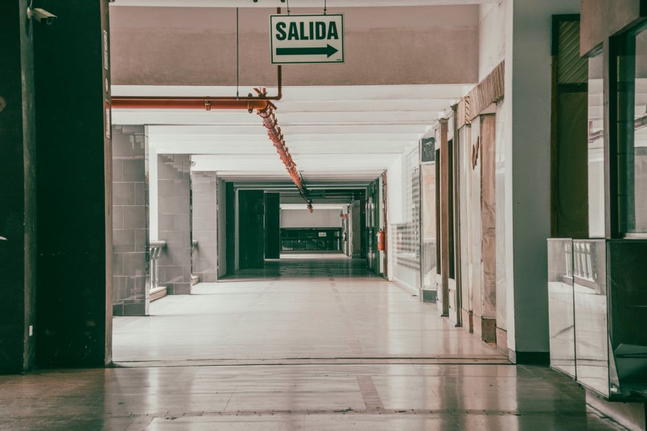 Imagen de un pasillo desierto con una señal de salida que muestra 'Salida', indicando una dirección.