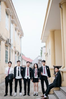 A group of high school students in uniforms standing outdoors against a school building backdrop.