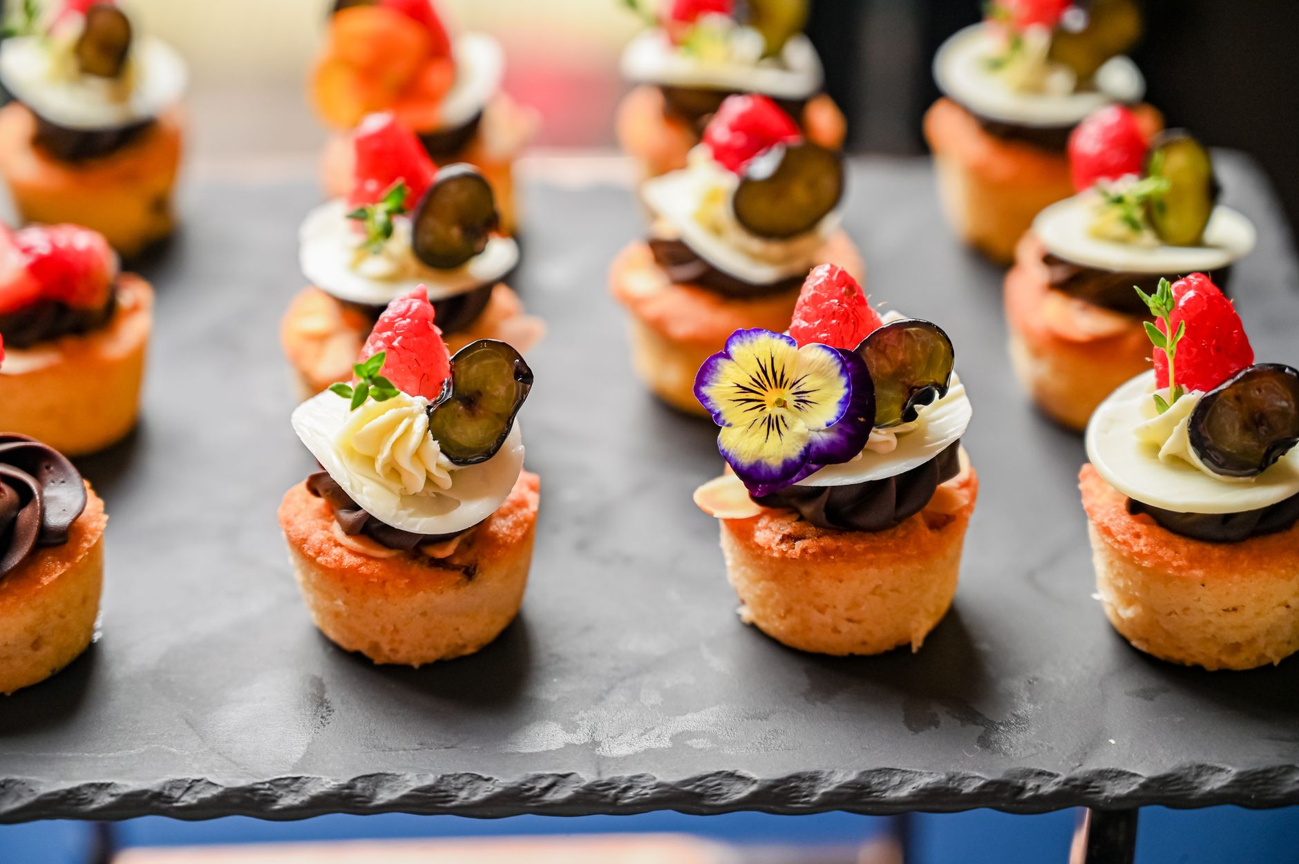 Delicious mini cupcakes topped with assorted fruits and flowers, perfect for elegant events.
