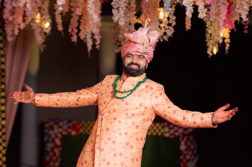 Free A groom joyfully poses at an Indian wedding, dressed in traditional attire with vibrant floral decor. Stock Photo