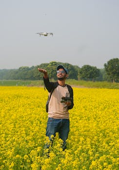A man operates a drone over a vibrant mustard field on a sunny day, blending technology with nature.