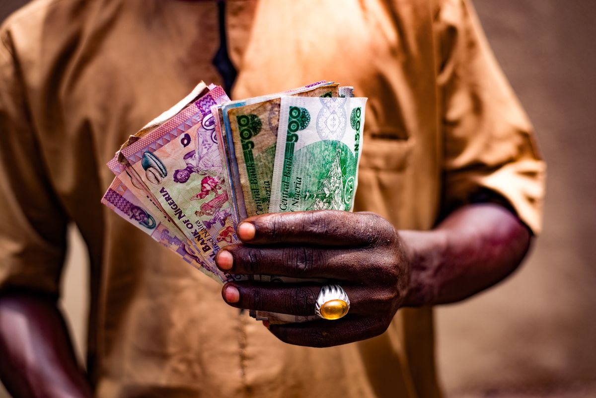 Nigerian man holding Nigerian currency while using modern financial services