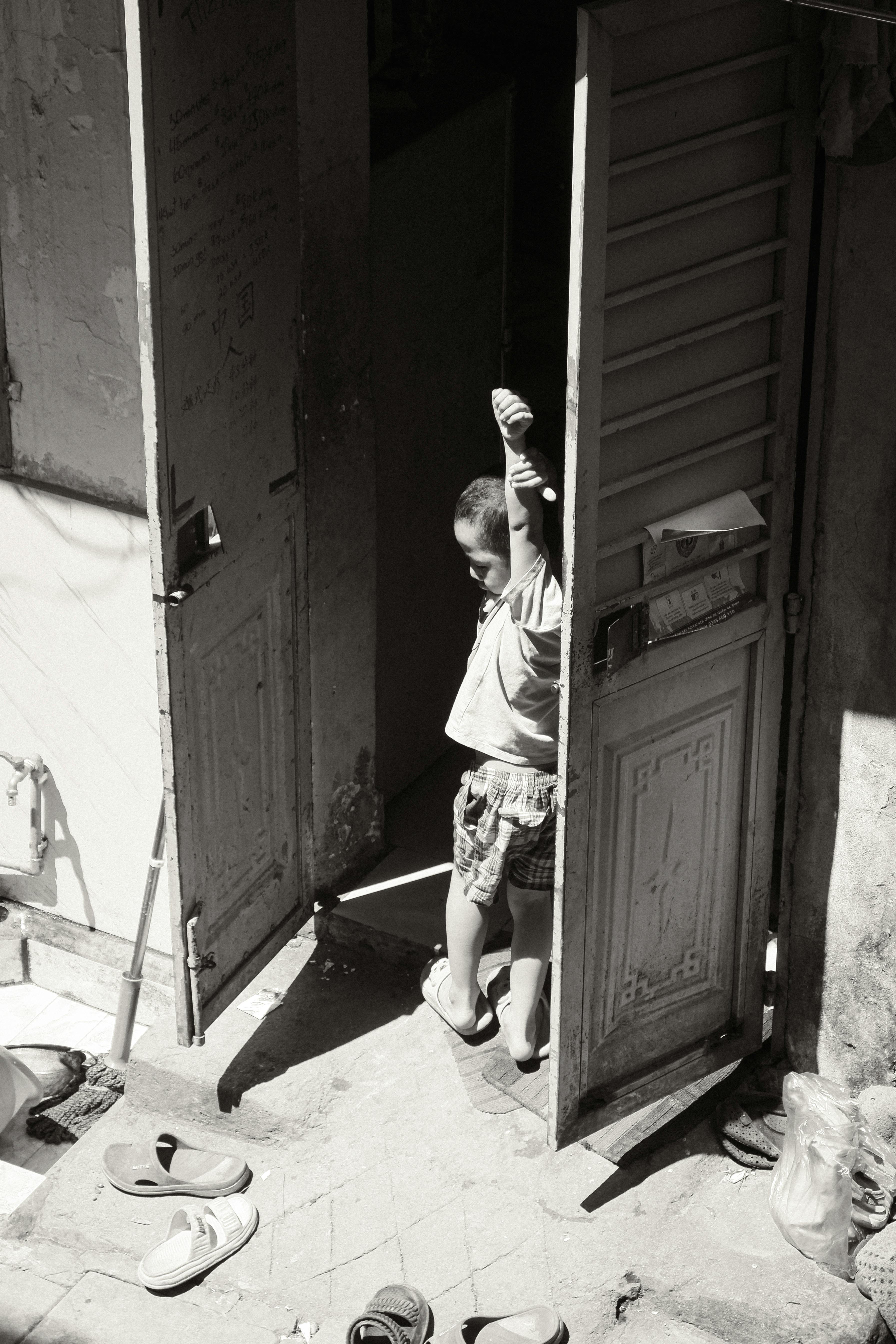 A young child standing in a sunlit doorway, capturing a candid moment in Hà Nội, Vietnam.