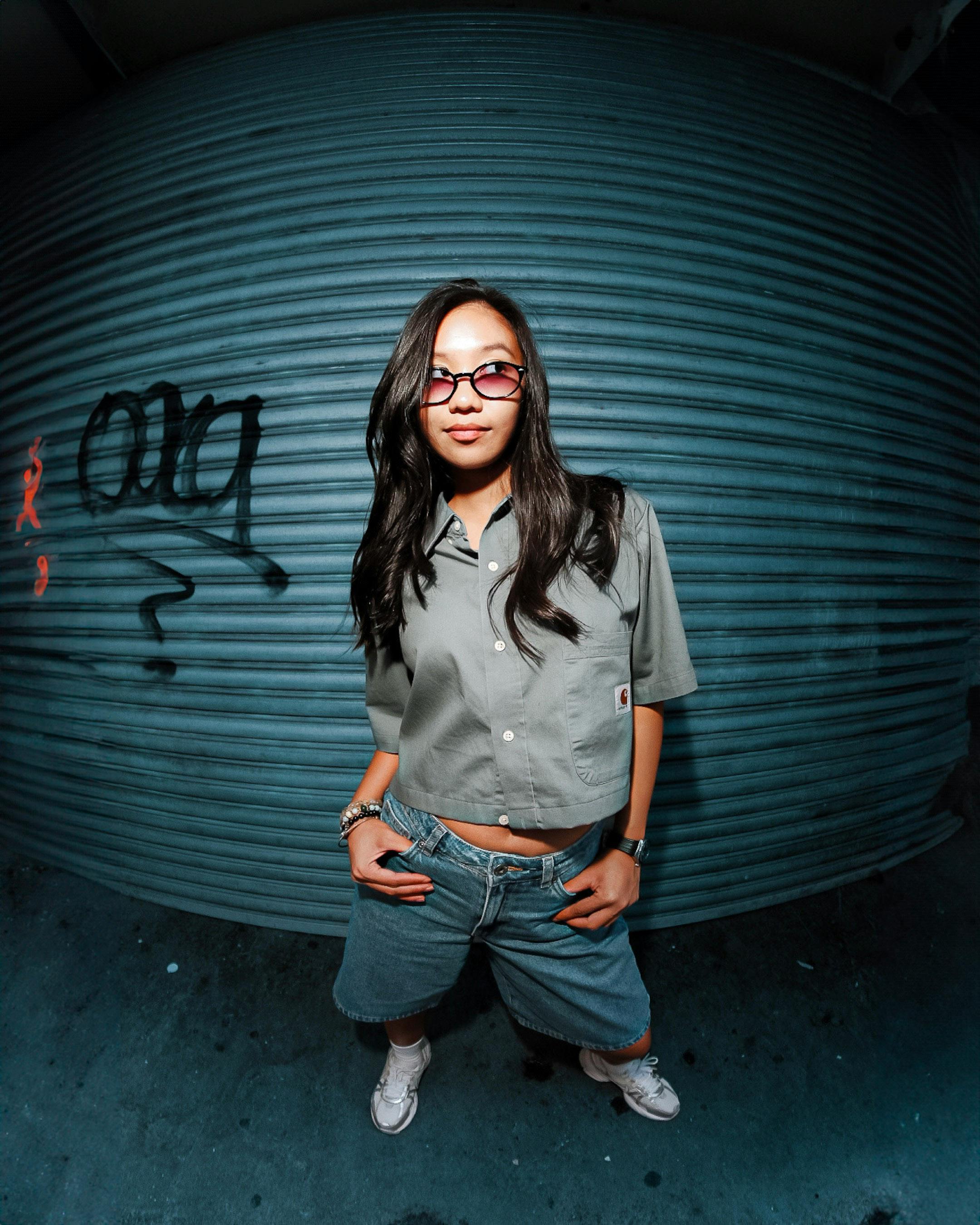 Stylish young woman stands confidently against graffiti backdrop.