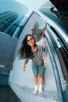 Young woman smiles in an urban setting with skyscrapers and a reflective mirror.