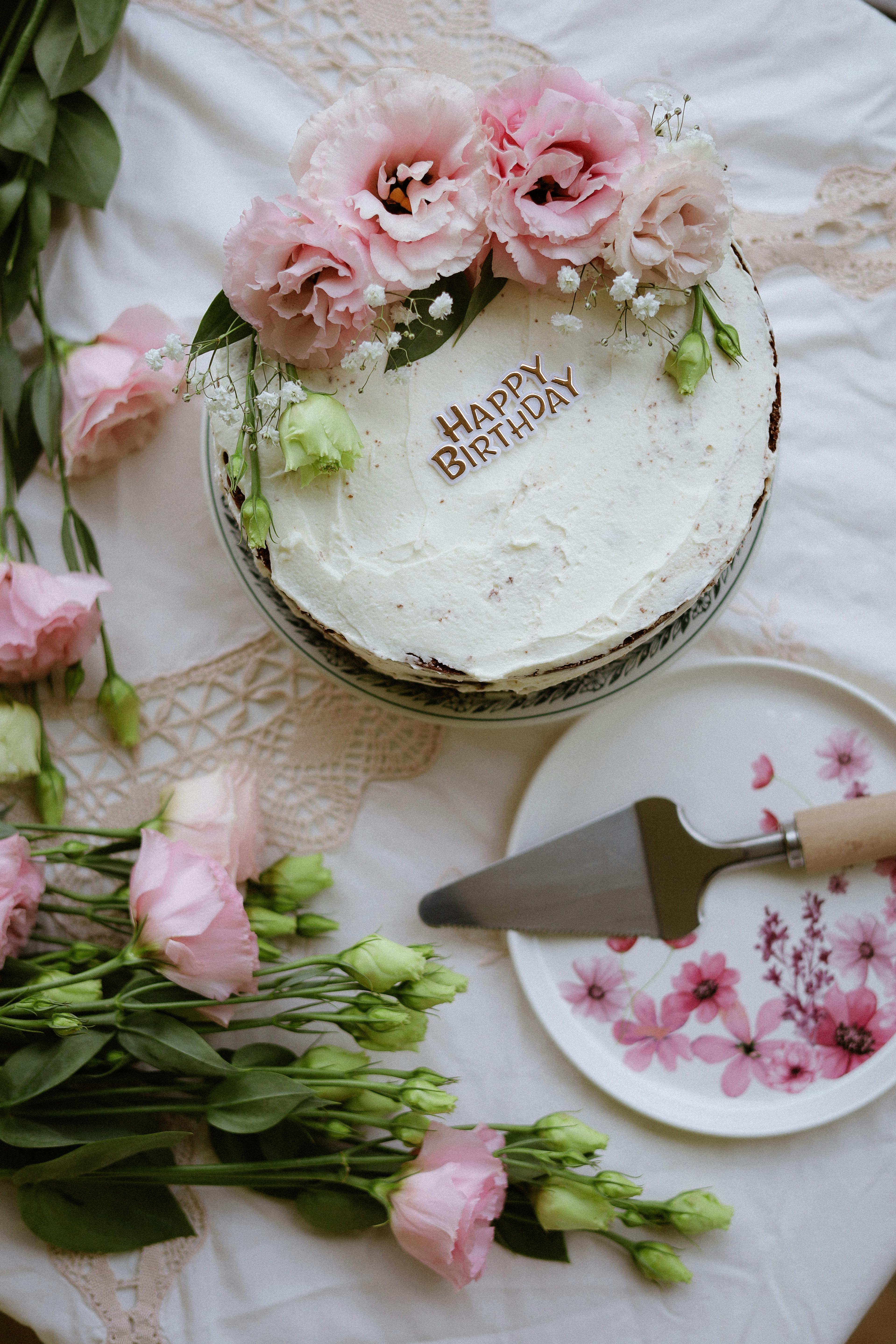 Free A beautifully decorated floral birthday cake with pink flowers on a lace tablecloth. Stock Photo