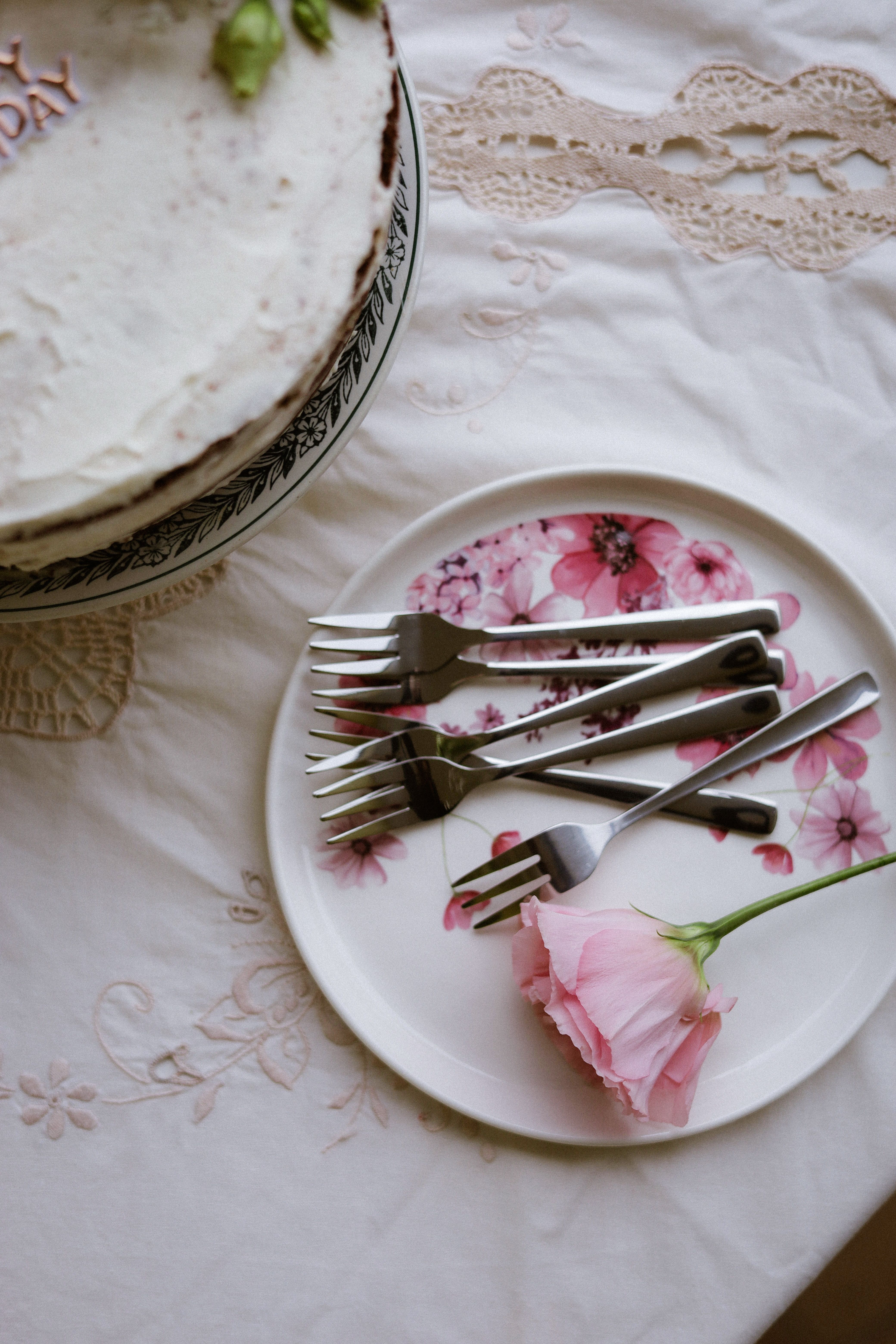A beautifully frosted cake with forks and pink flower on a floral plate.