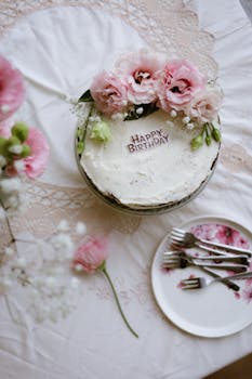 A beautiful birthday cake adorned with pink flowers on a festive table setting.