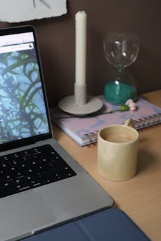 A serene workspace featuring a laptop, candle, hourglass, and coffee cup for productivity.