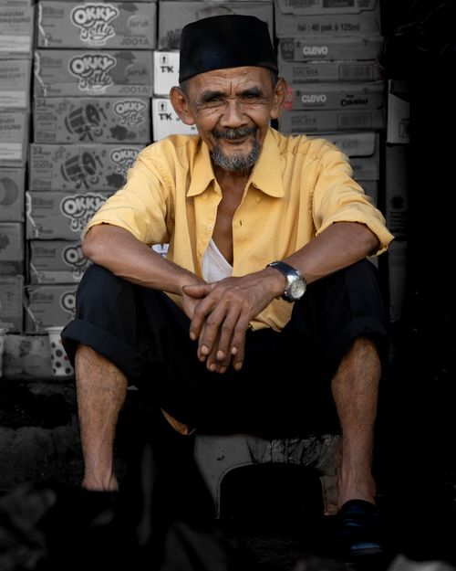 Free An elderly man with a warm smile sitting in front of boxes in West Java, Indonesia. Stock Photo