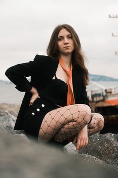 Confident woman in fishnet tights poses by the seaside rocks.