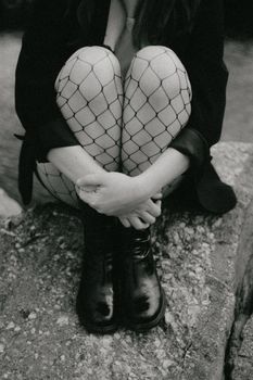 Stylish black and white capture of a woman seated in fishnet tights and boots, creating a moody atmosphere.