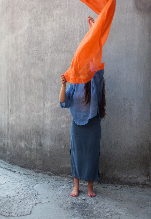 Free Woman in flowing attire holding orange scarf near a concrete wall. Stock Photo
