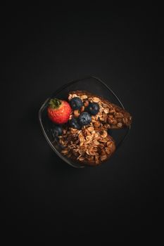 A healthy bowl of granola topped with fresh strawberries and blueberries.