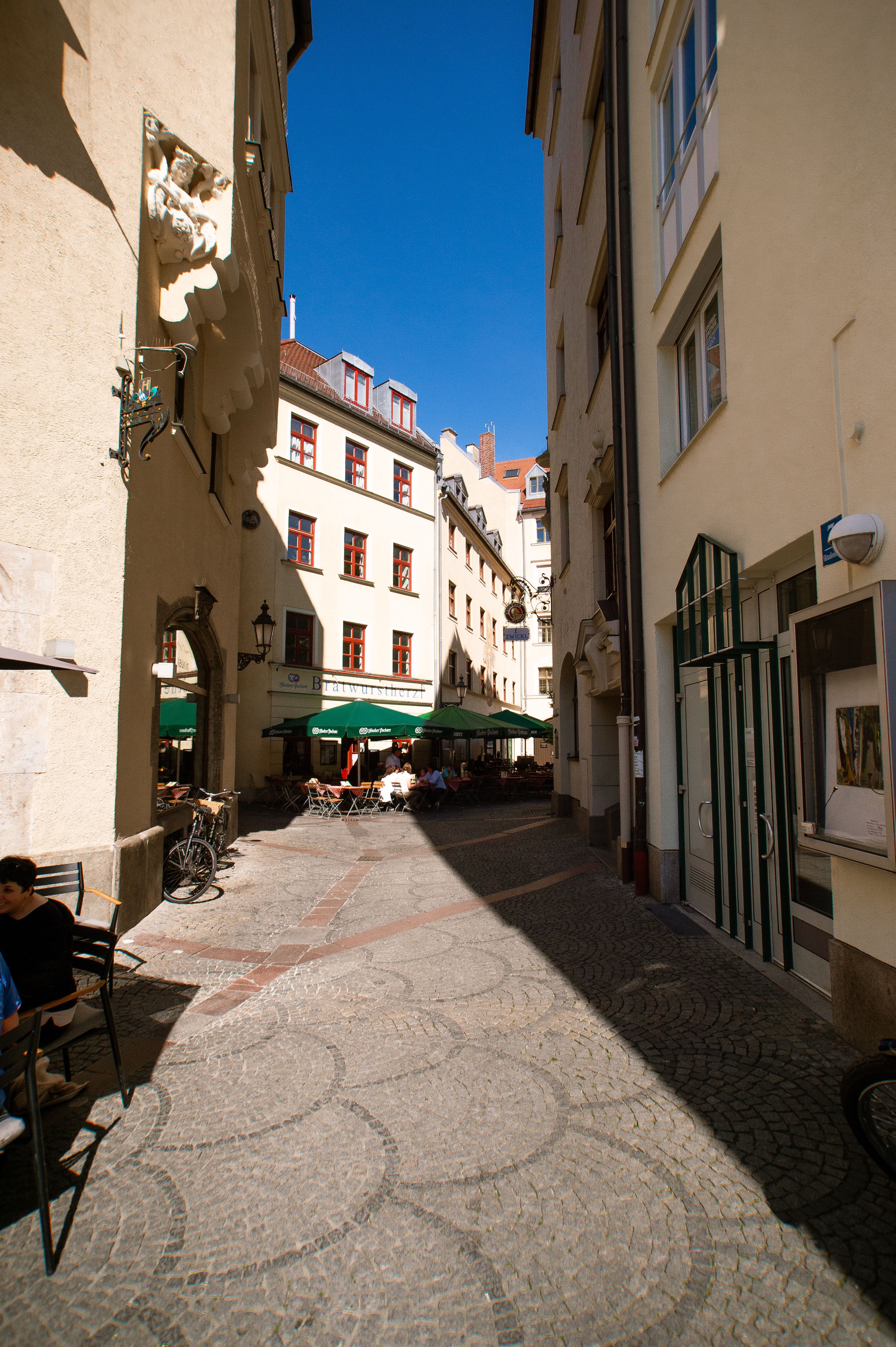 Charming European alley with cobblestone path, outdoor cafe seating, and historic architecture.