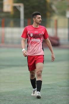 Young male soccer player in red uniform walking on field.