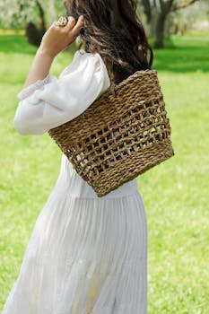 Stylish woman in white dress holding a straw bag in a sunny park setting.