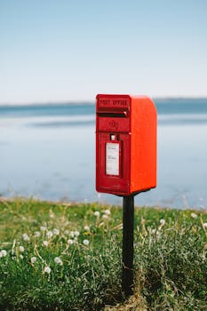 Red post box by the scenic Avoch seaside in Scotland, against a blue sky backdrop.