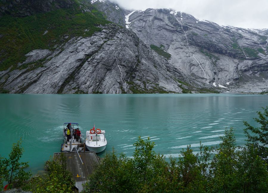 Stunning turquoise water with a boat docked at a fjord surrounded by rugged cliffs in Norway.