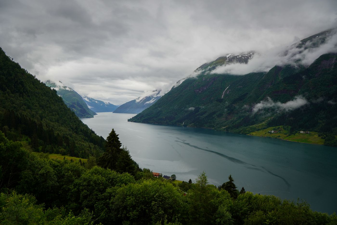 Steep green mountains dropping into a fjord on the coast of Norway under a cloudy sky