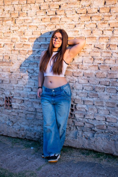 Free Casual portrait of a young woman standing confidently against a brick wall outdoors. Stock Photo