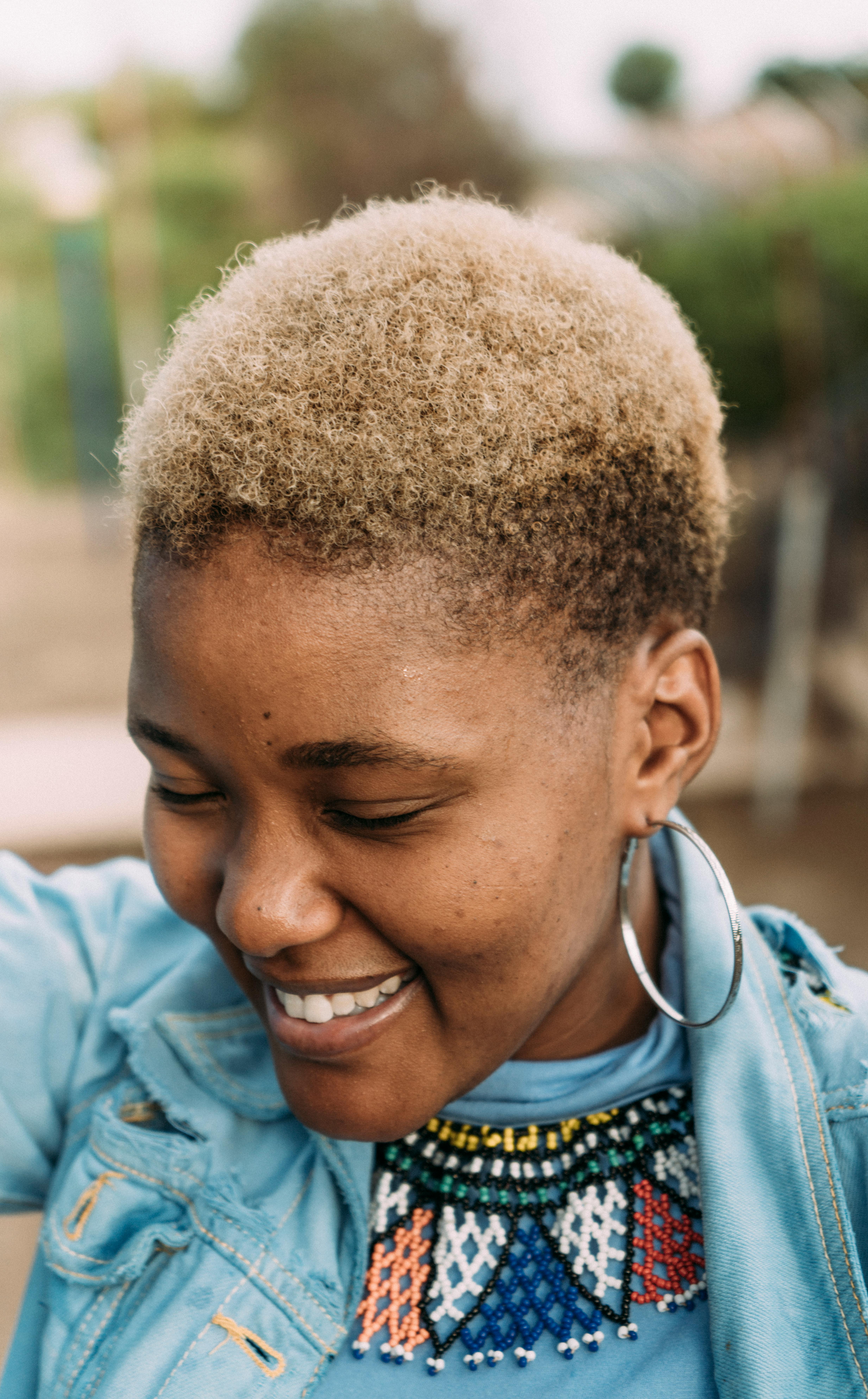 Portrait of a smiling woman with a short afro hairstyle, showcasing vibrant beaded jewelry, captured outdoors in Namibia.